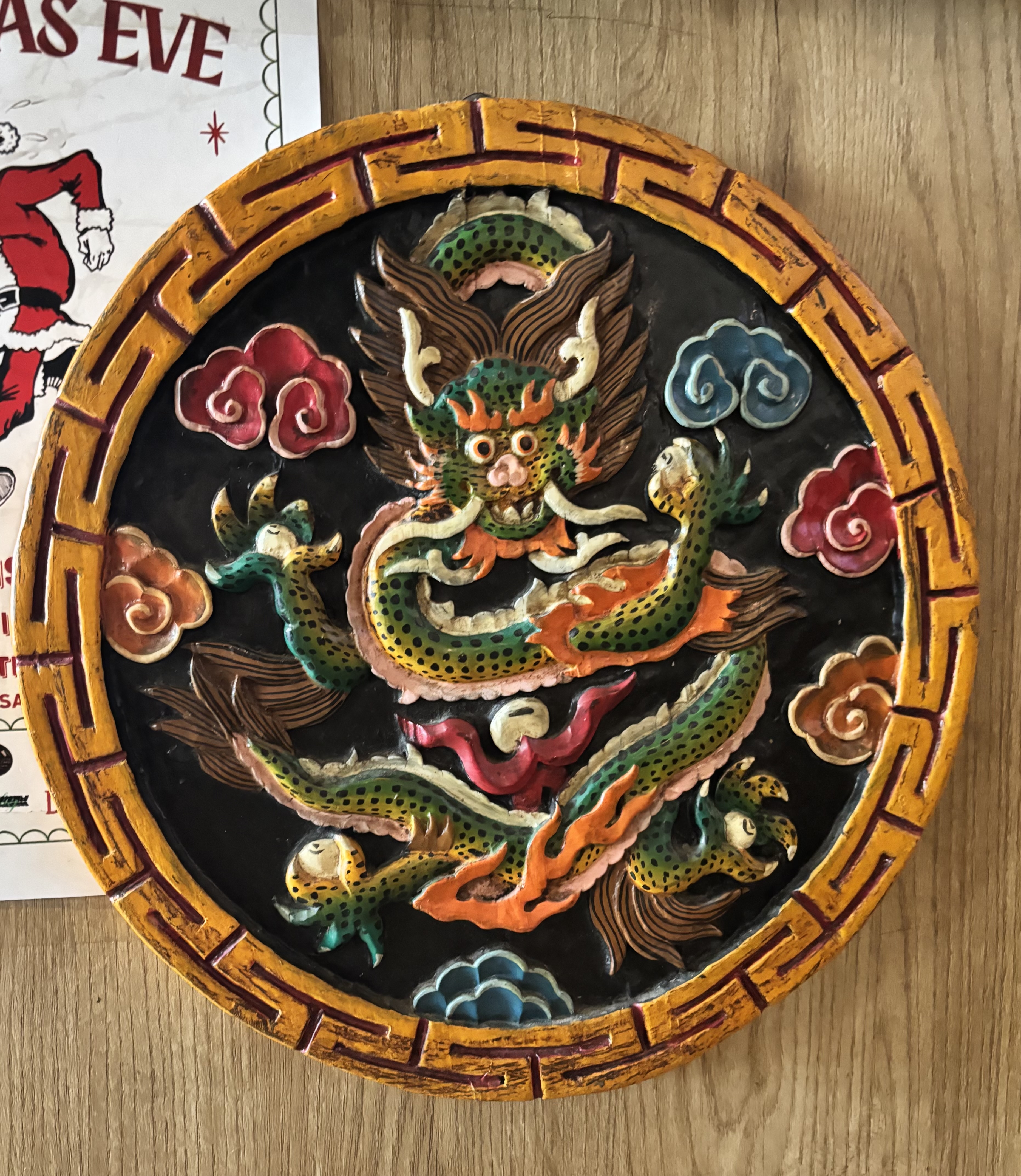 Round, ornate dragon carving with vibrant colors on a wooden surface. The dragon appears dynamic, surrounded by colorful clouds, exuding an energetic, mythical aura.