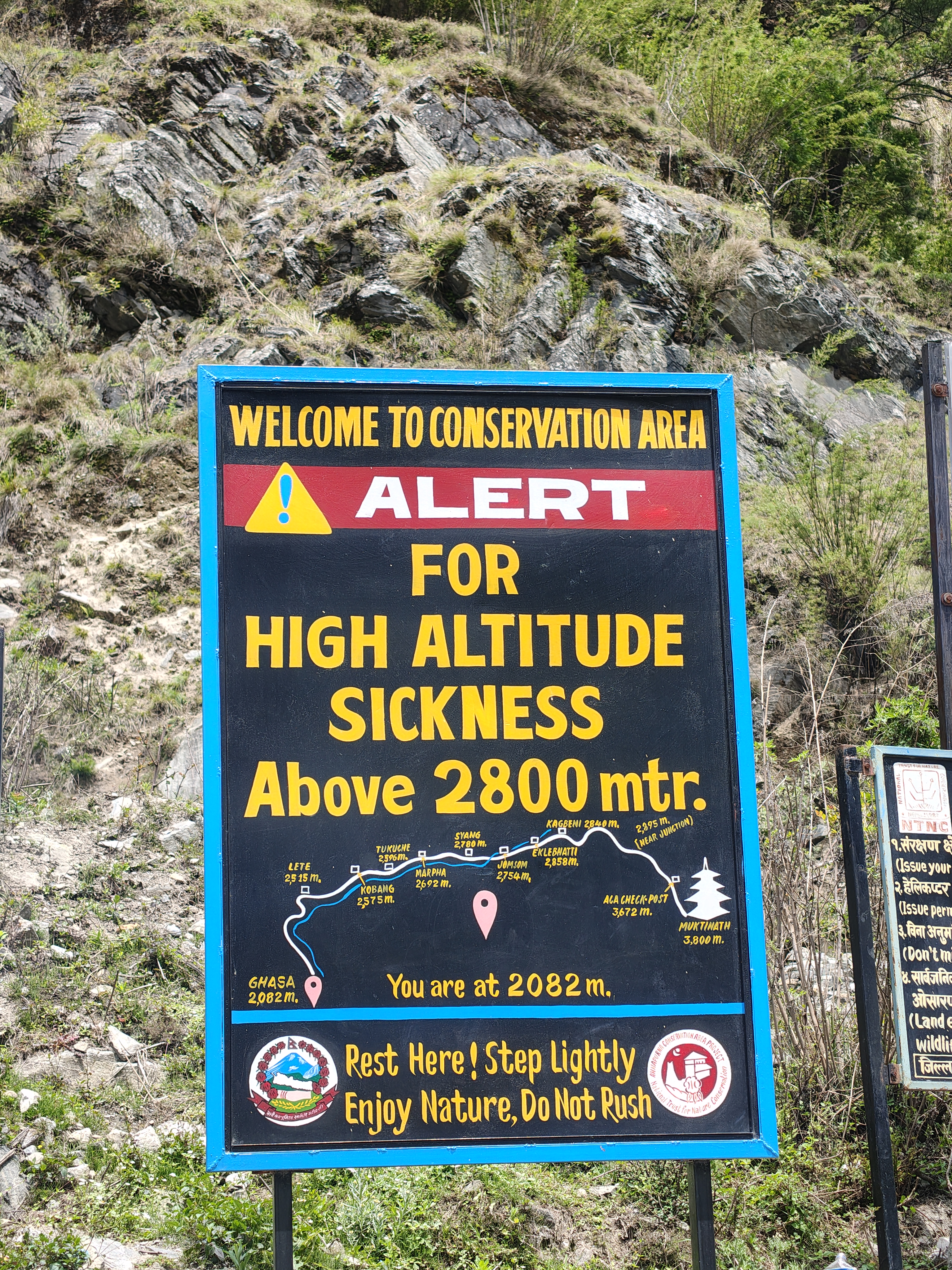 Sign warning of high altitude sickness above 2800 meters in a conservation area. Includes a map, elevation points, and safety advice. Rocky, green background.