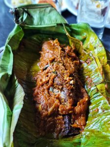 A fried fish coated in batter held in a in banana leaf.
