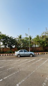 A silver car is parked in an empty parking lot under a clear blue sky. 