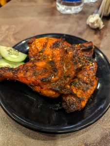 A close-up of grilled chicken pieces on a black plate, coated in a charred, spicy marinade.