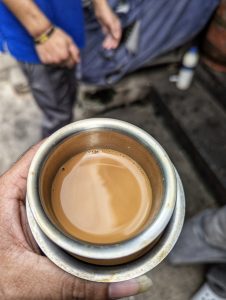 A close-up of a hand holding a metal cup of brown filter coffee with a reflective surface.