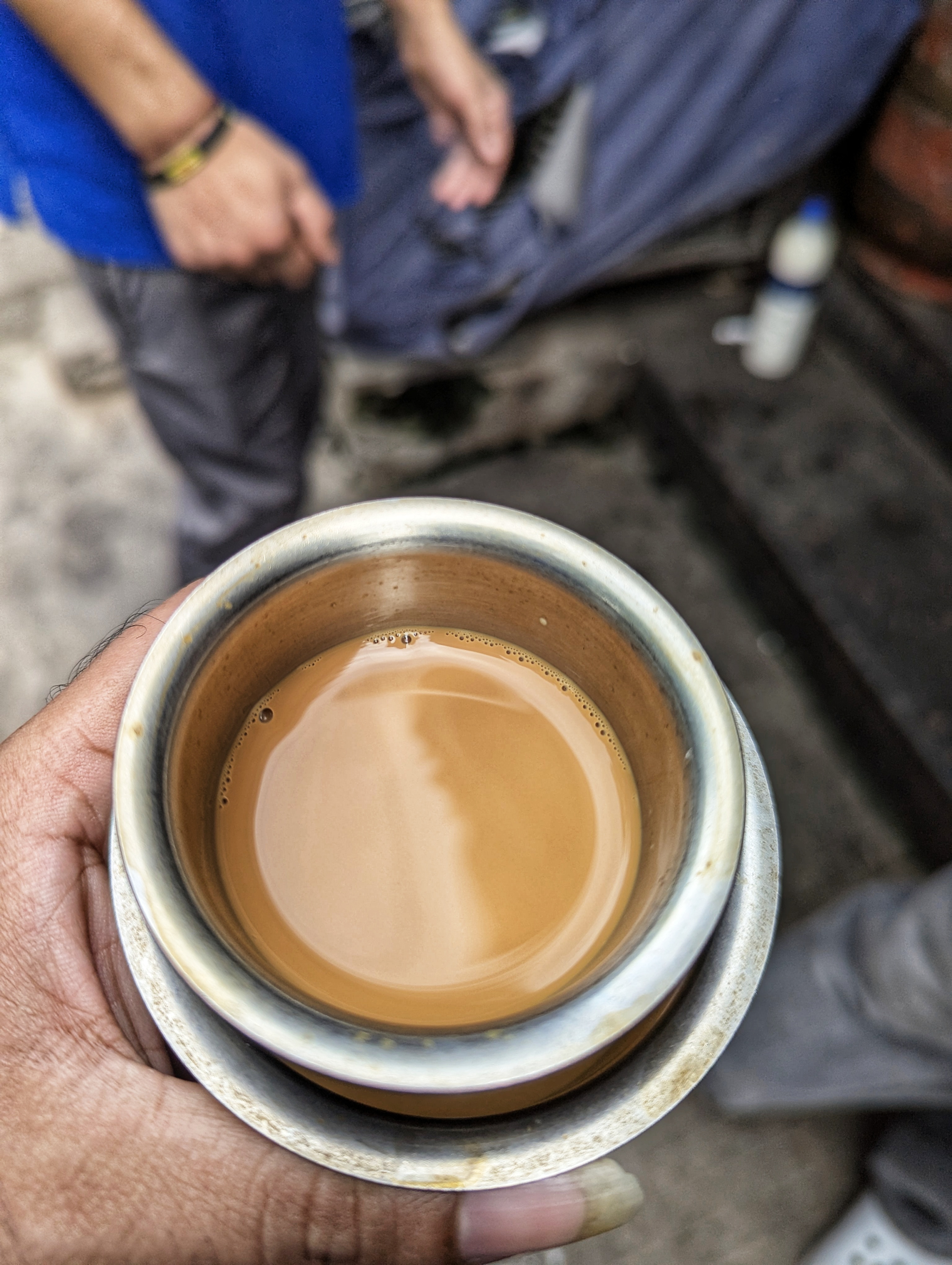 A close-up of a hand holding a metal cup of brown filter coffee with a reflective surface.