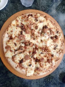 A round pizza topped with melted cheese, sliced sausage, and mushrooms on a wooden board.