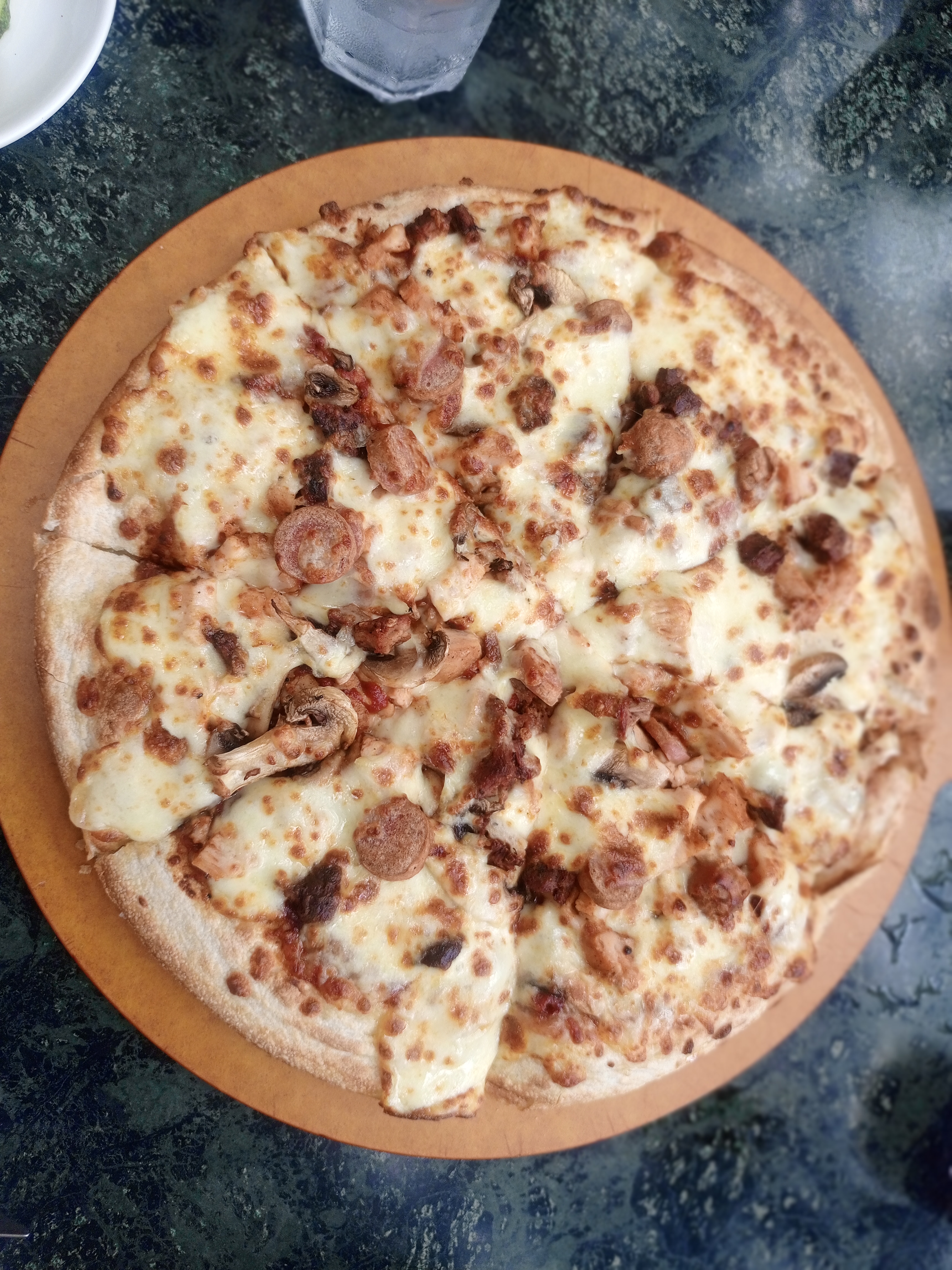 A round pizza topped with melted cheese, sliced sausage, and mushrooms on a wooden board.