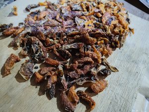 Slices of locoto drying on a wooden surface, being prepared to be ground into locoto powder. Their reddish tones and wrinkled texture reflect the artisanal process of preserving and concentrating the spicy flavor.