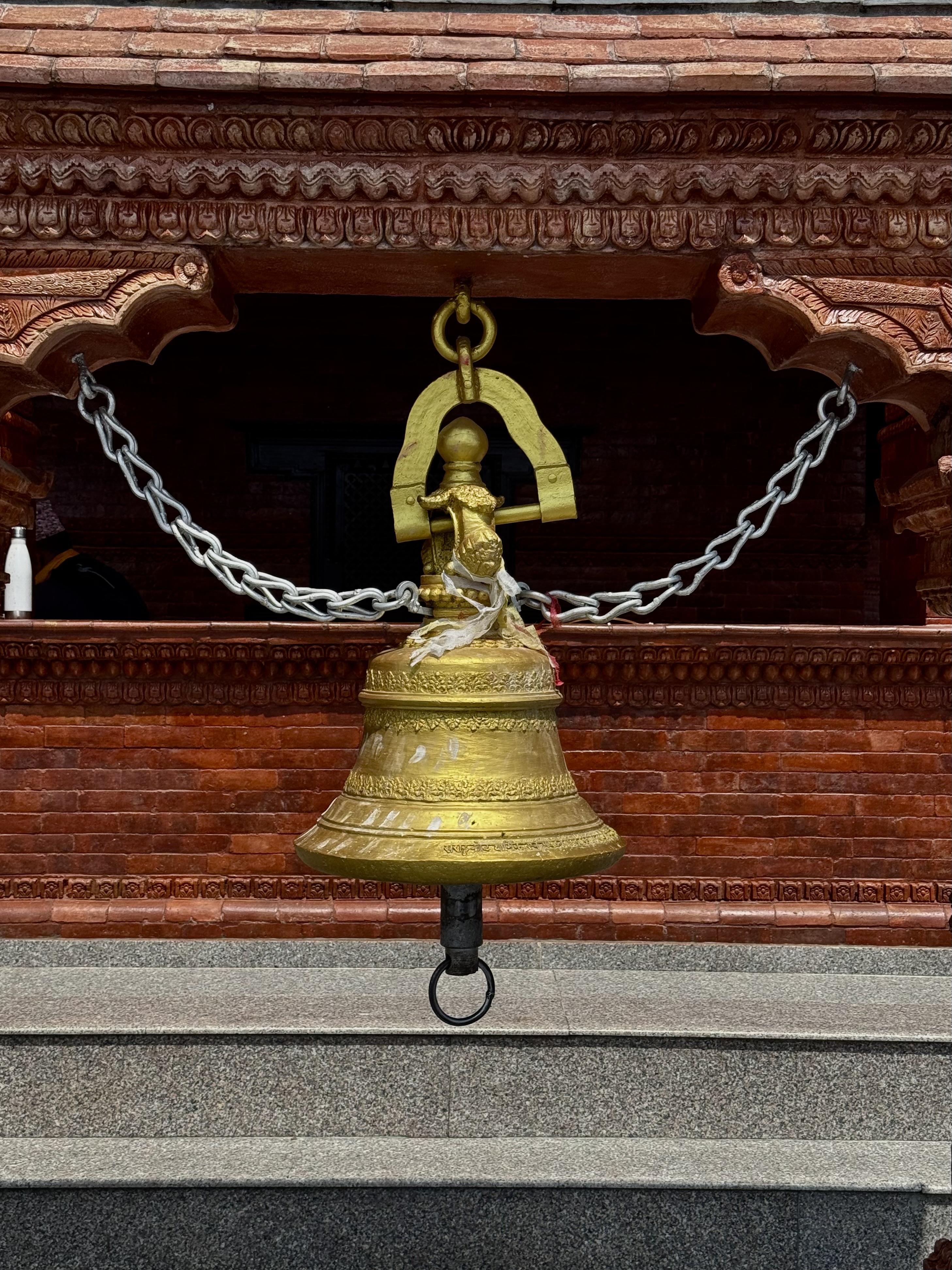 A golden bell which is hold by a gare like structure and two heavy iron chains.