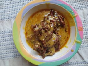 A colorful bowl of creamy kari pakora in golden curry sauce, served on a textured cloth, warm and comforting.