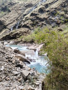 A serene mountain landscape with a small cascading waterfall flowing into a clear, blue stream.