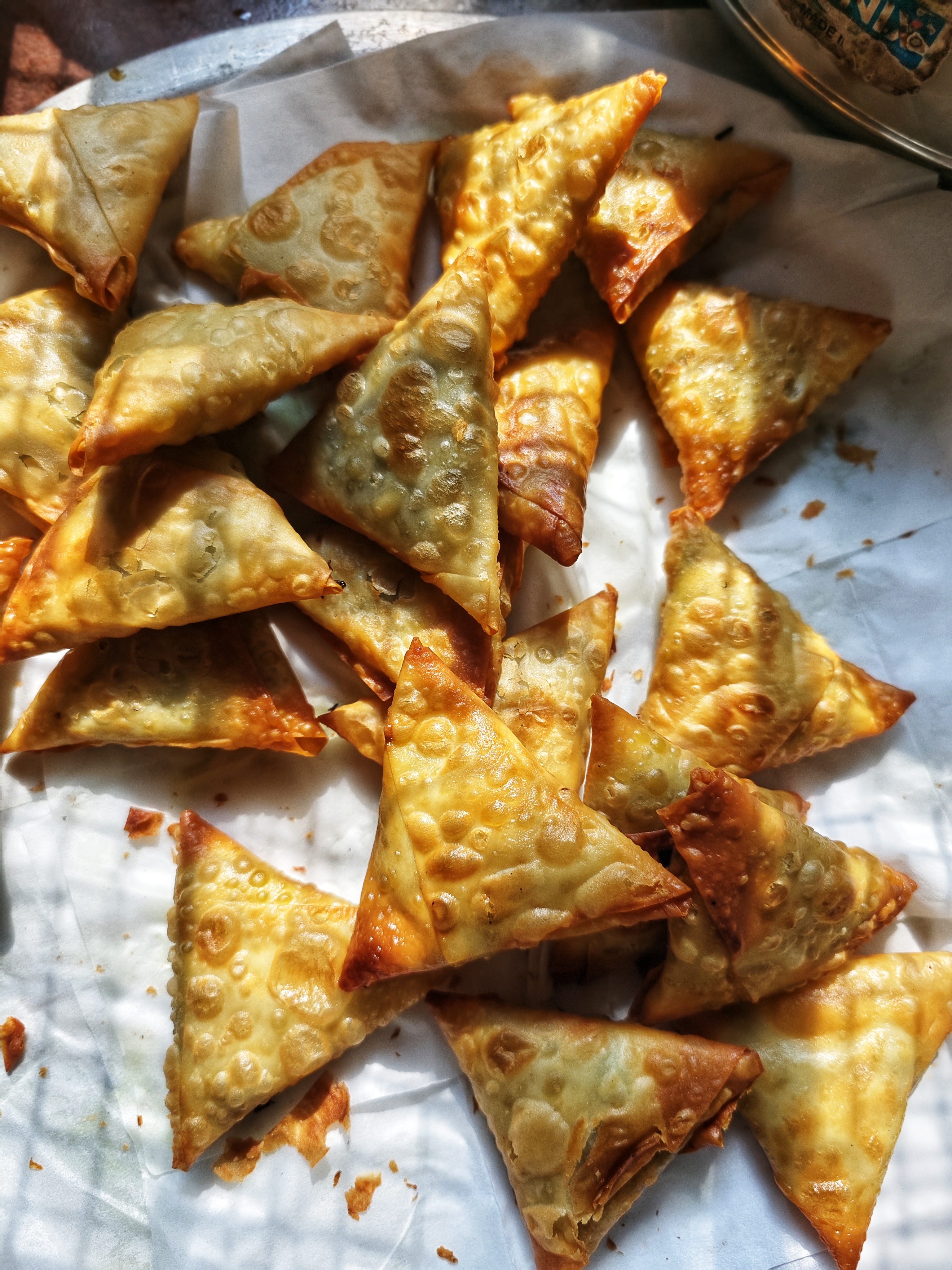 A close-up view of freshly fried samosas arranged on a tray lined with parchment paper.