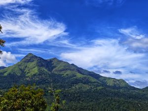 Lush green mountains under a vibrant blue sky with wispy clouds. Dense forest covers the slopes, creating a serene and majestic landscape.