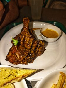 
A plate of grilled chicken leg, garnished with a small green flag, next to a bowl of sauce.