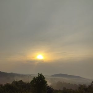 Sunrise over a misty landscape with gently rolling hills.