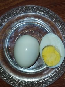 A boiled egg, whole and halved, sits on a clear textured glass plate. 