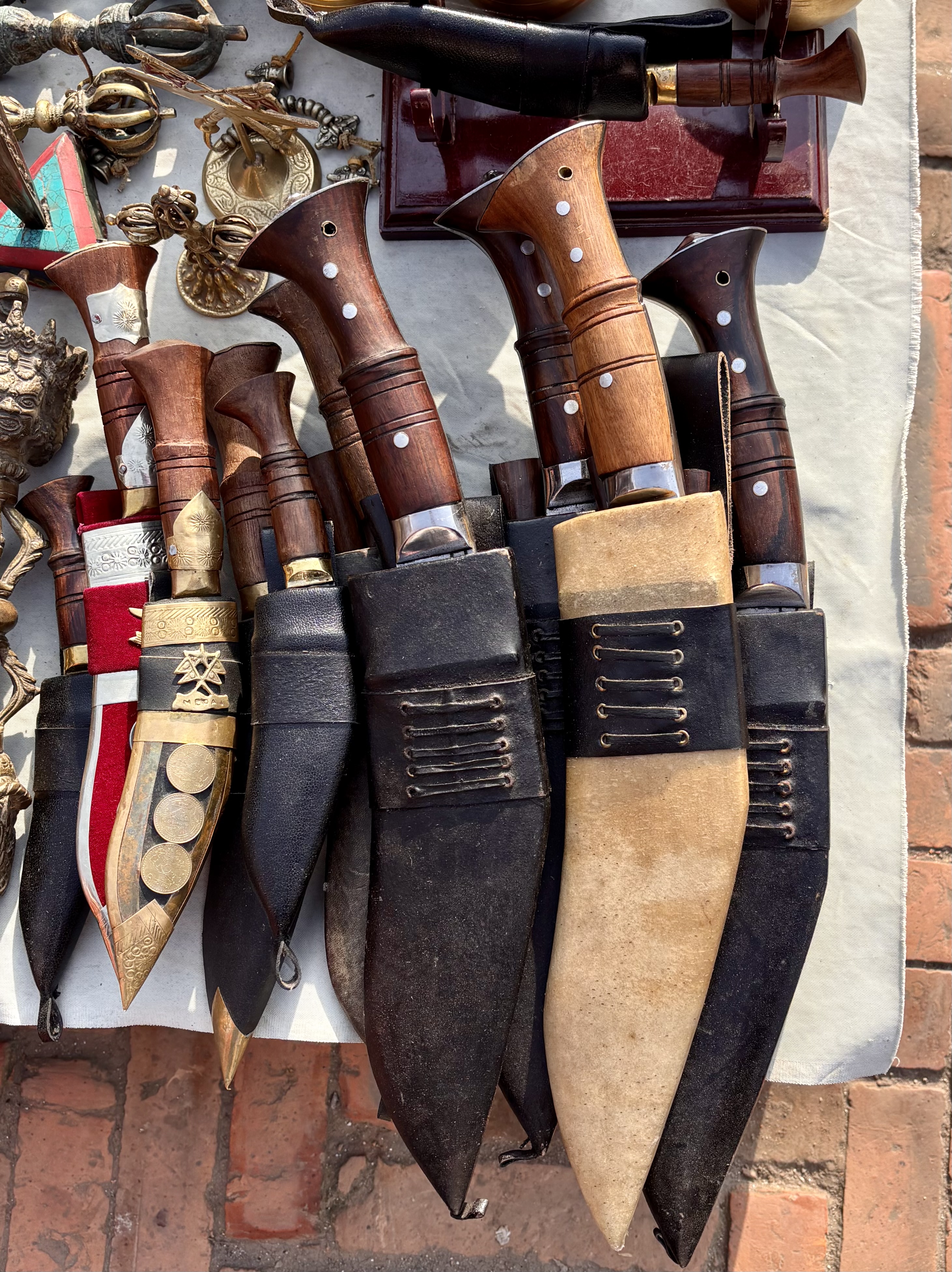 Display of traditional knives with wooden handles and decorative sheaths in black and tan on a table; some ornate brass items are also visible.