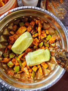 A stainless steel bowl of chopped green and yellow mango masala sprinkled with red chili powder.