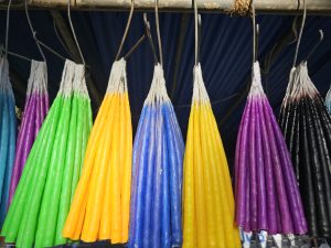 Bright, colorful candles hang neatly in a row at a market stall, creating a vibrant and eye-catching display. Captured in Bandra, Mumbai. 