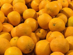 A pile of fresh vibrant oranges with textured skin and small natural blemishes.