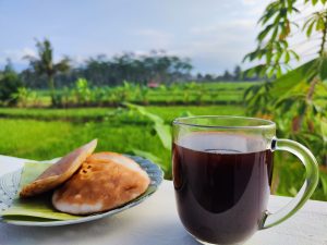 A glass cup of dark coffee sits on a white ledge next to two golden-brown pastries on a plate with green leaves