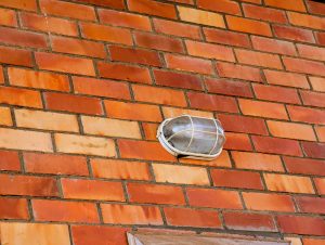An outdoor light fixture with a metal cage cover is mounted on a red brick wall, adding a simple industrial touch.