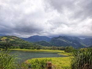 Lush green hills surround a river under a dramatic, cloudy sky.