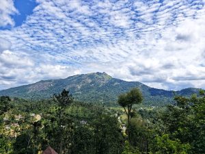 Mountain landscape under a sky with scattered clouds. Lush greenery covers the foothills, suggesting a serene and vibrant natural environment.
