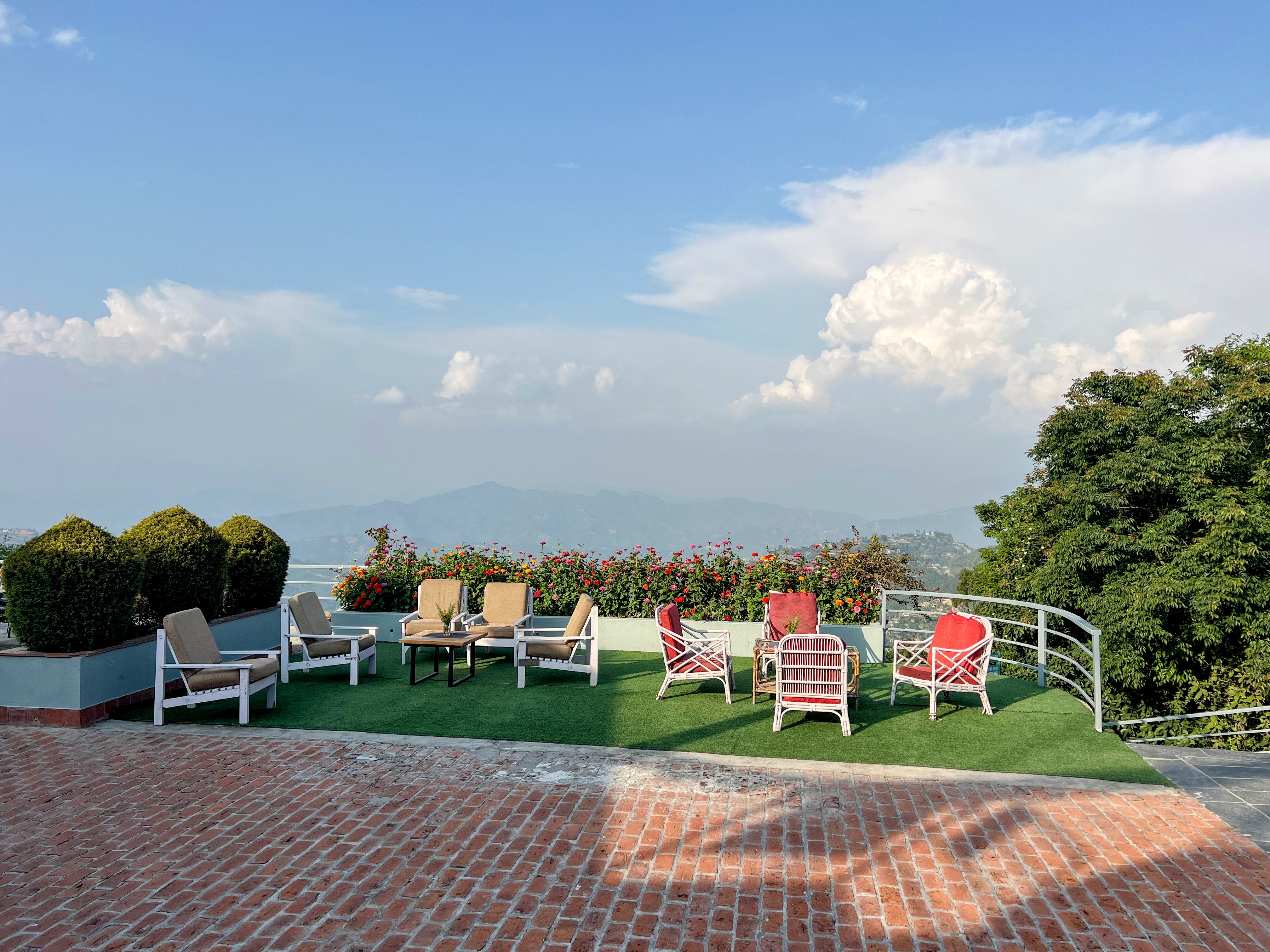 An outdoor seating area with red and white chairs on artificial green turf, overlooking a panoramic view of distant mountains under a blue sky.