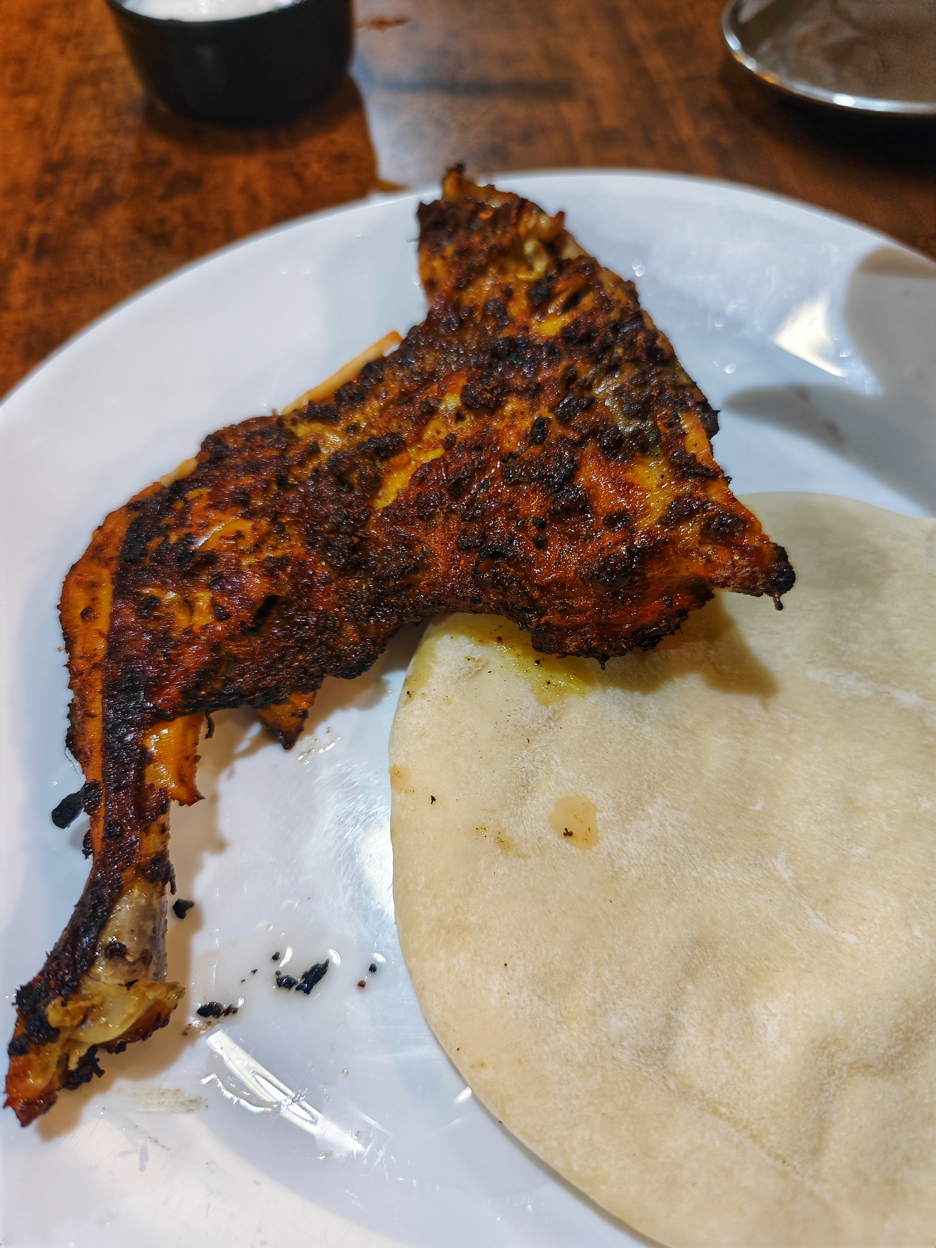 Grilled chicken with a crispy charred surface beside a soft flatbread on a white plate.