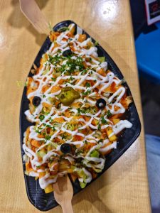 
A black, oval-shaped platter filled with loaded fries topped with a variety of ingredients. 