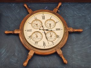 A beautiful vintage wall clock designed like a ship’s steering wheel, showing multiple world time zones. The warm wooden frame and classic Roman numerals give it a timeless nautical look. Captured indoors in Kurla, Mumbai.