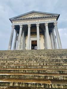 A majestic neoclassical church (Chiesa della Gran Madre di Dio) with tall pillars and long stone steps creates a powerful and dramatic scene under dark clouds in Turin (Torino), Italy. 