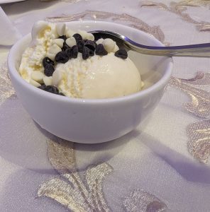 A bowl of vanilla ice cream topped with chocolate and white chocolate chips sits on a decorative tablecloth.