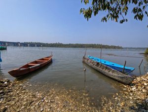 A tranquil riverside scene featuring three boats: a long, narrow red boat, a blue boat, and a dark, weathered boat. 