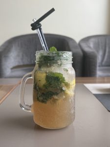 A refreshing drink in a mason jar, filled with iced lemonade, mint leaves, and lemon slices. One black straw pokes out. 