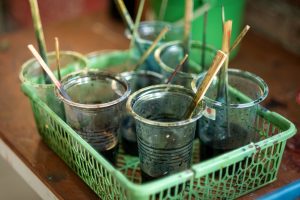 A plastic tray with several plastic cups containing dye used to create batik fabrics.
