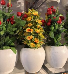 Three white pots with vibrant artificial flowers, featuring yellow blooms and red berry accents, creating a colorful and lively arrangement.