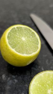 Close-up of a freshly cut lemon half on a dark surface, with a knife blurred in the background.
