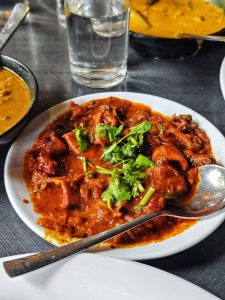 A plate of spicy red stewed koonthal (squid) topped with fresh green cilantro, served with yellow curry and a glass of water in the background.
