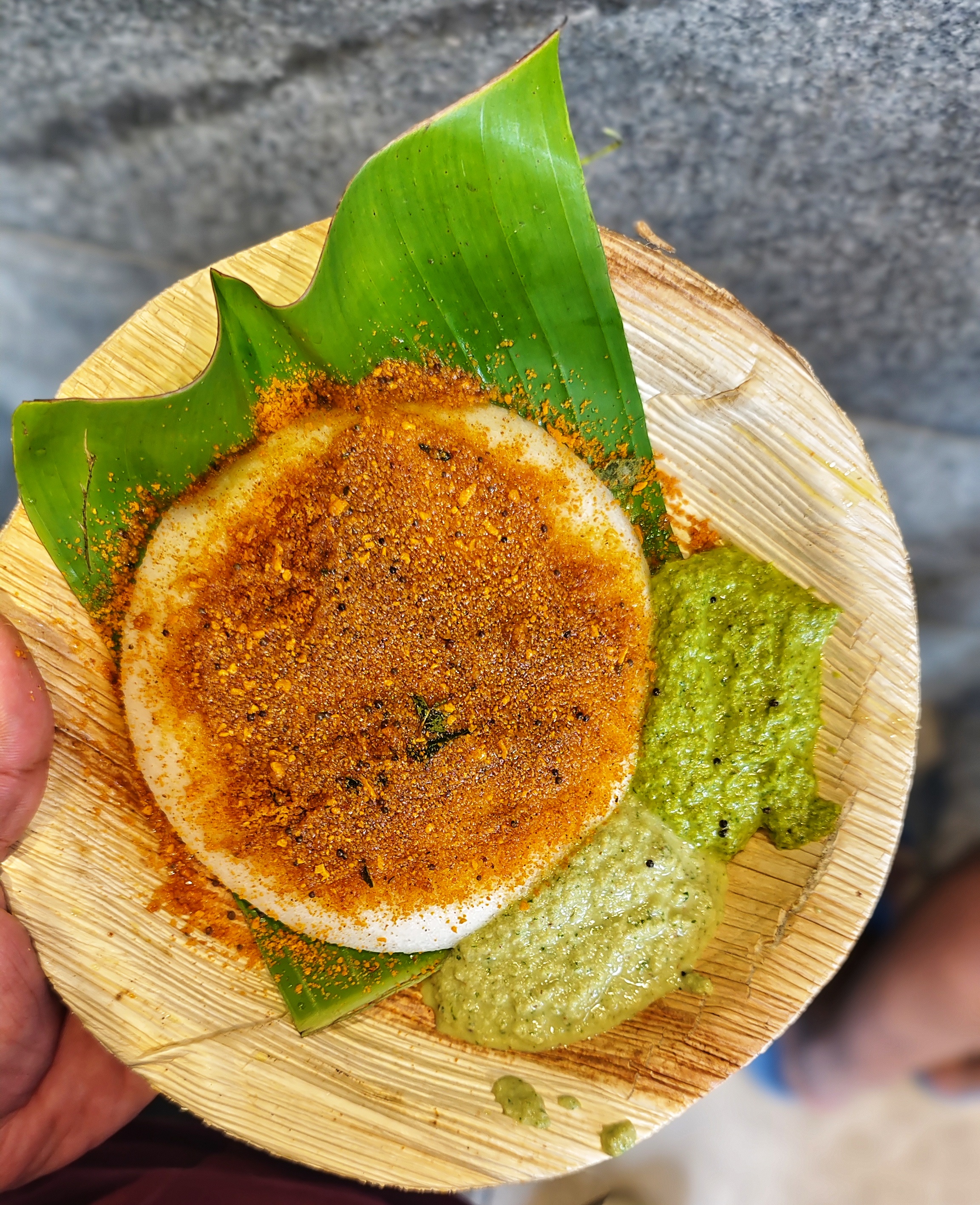 A round white dosa sprinkled with spices, served on a banana leaf in a bamboo plate as ghee podi idli.