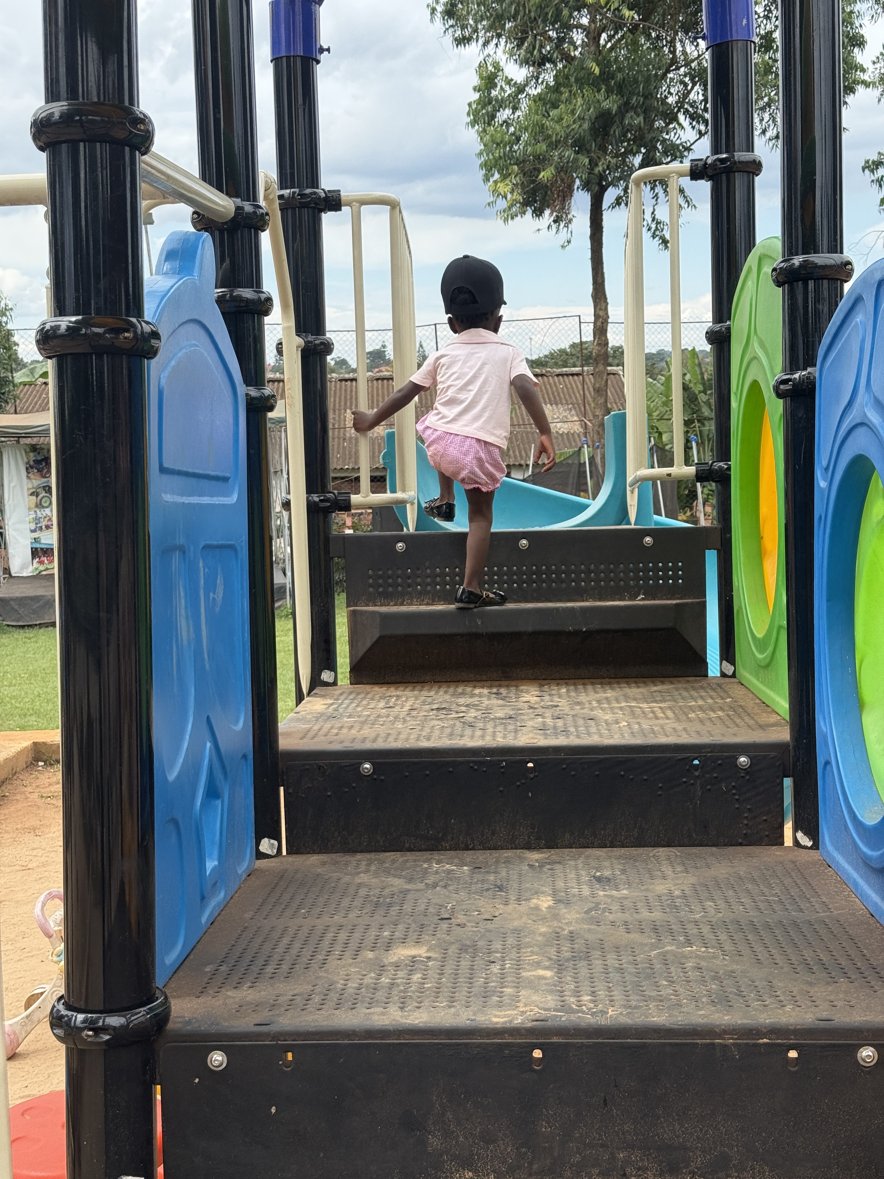 A child is climbing a set of steps on a playground structure. The playground features colorful elements, including green and blue climbing panels on the sides.