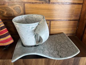 A light blue ceramic mug with a webbed, crackled pattern sitting on a matching, wavy-edged saucer.
