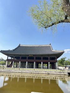 Traditional Asian pavilion with a tiered roof, set by a tranquil waterway under a bright blue sky.