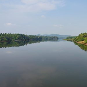 A calm river reflecting a cloudy sky, with green vegetation on both sides.