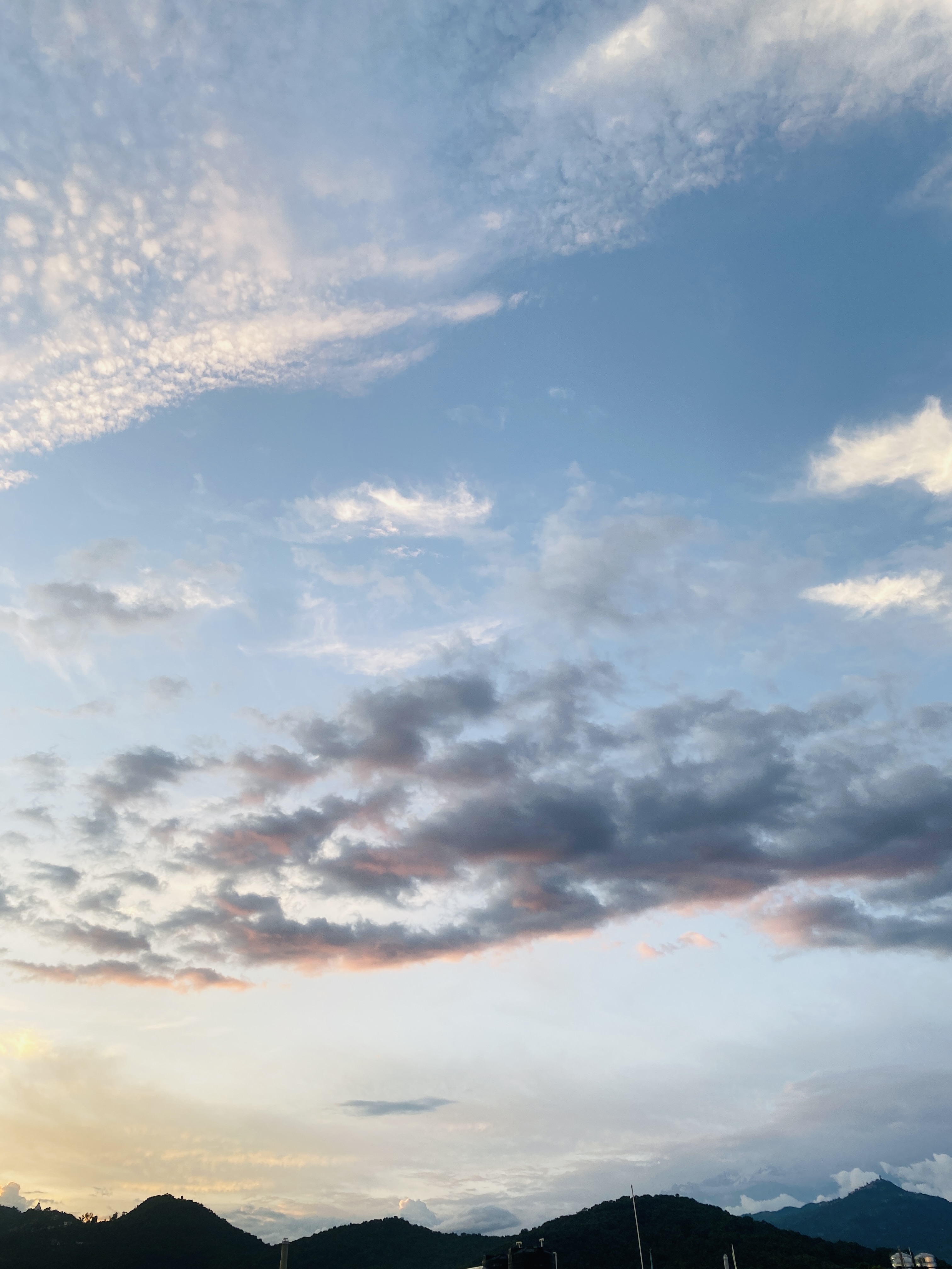 A scenic view of the sky featuring a gradient of soft blue and white clouds, with hues of pink and orange near the horizon.