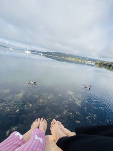 A picture of the feet of a couple at the edge of the sea, where two floating ducks are visible.

