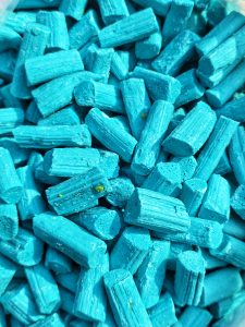 A close-up of small cylindrical blue candy pieces in a turquoise shade.