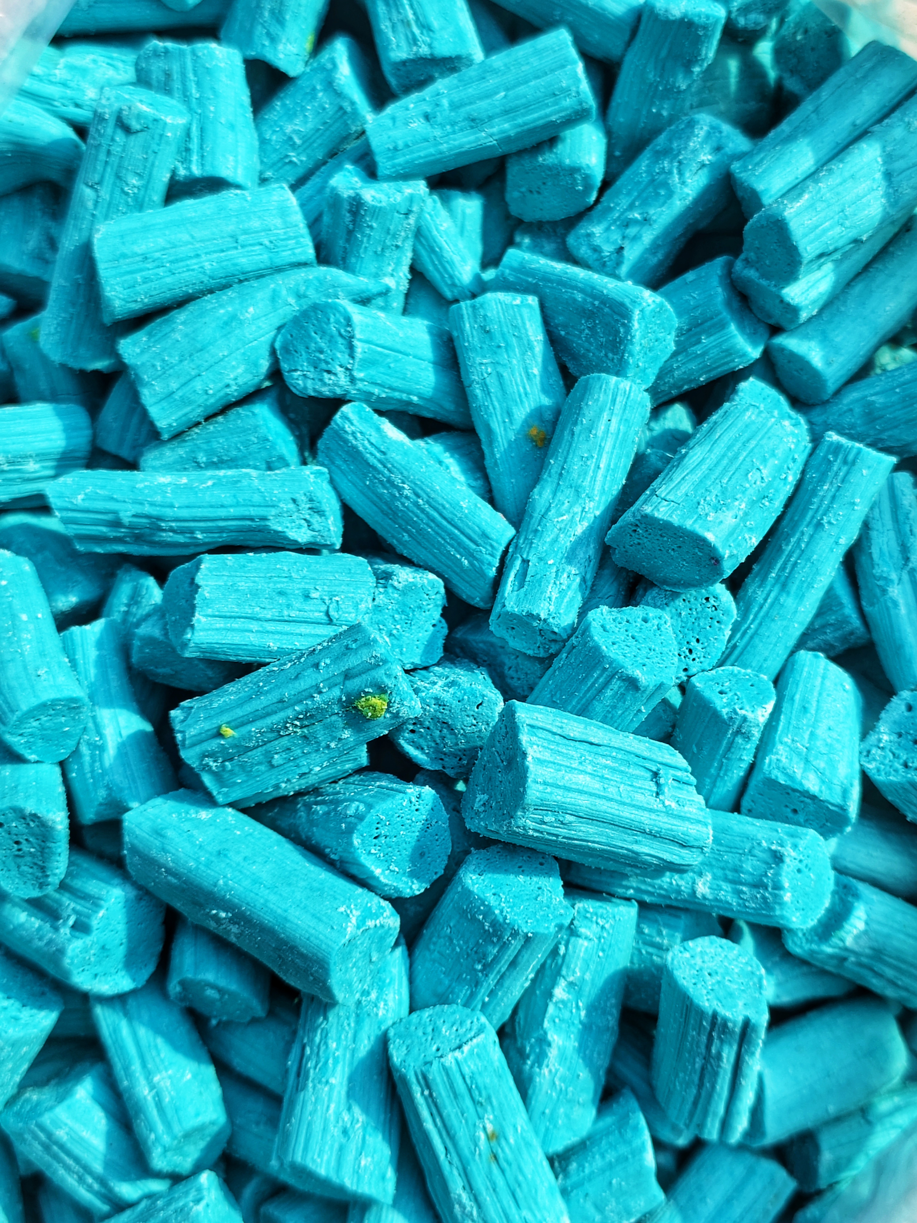 A close-up of small cylindrical blue candy pieces in a turquoise shade.