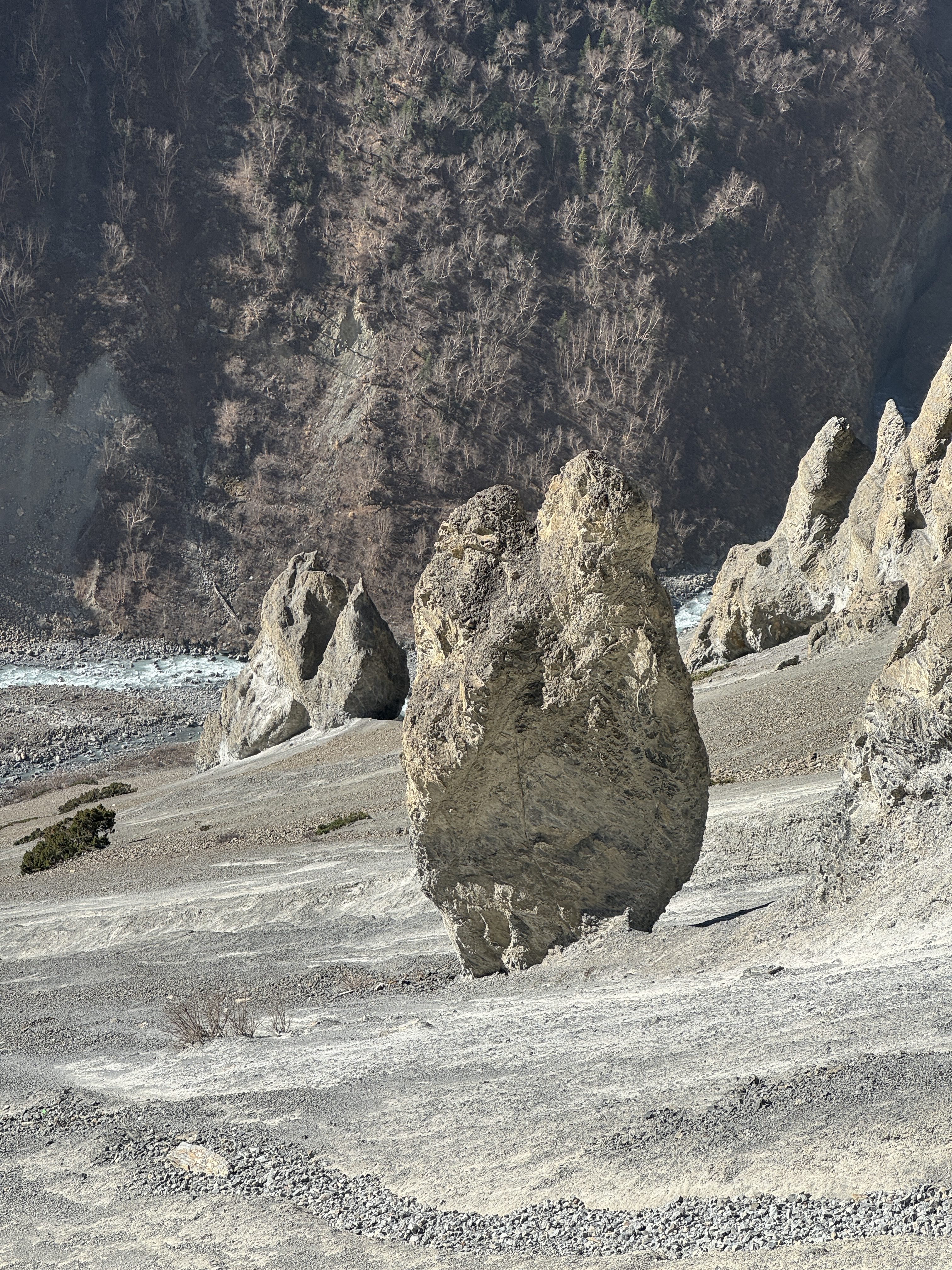 A prominent eroded rock formation and geological spires standing on a grey gravelly slope above a mountain river valley in the Annapurna region.