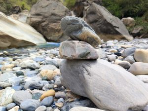 Cairn stones are balanced on a riverbank covered with small rocks.