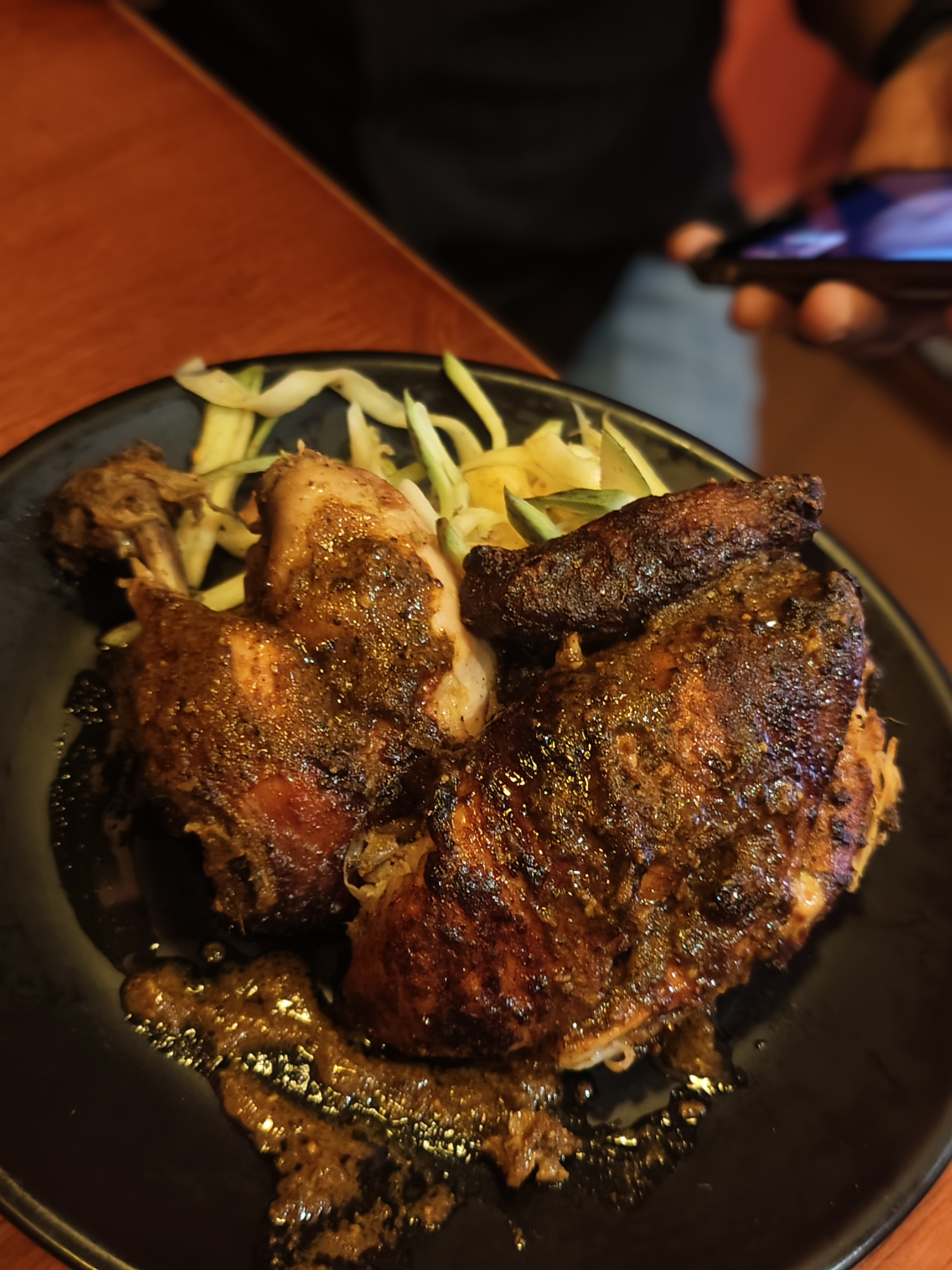 Grilled chicken pieces on a black plate with a glossy, spicy marinade, served with sliced cucumbers
